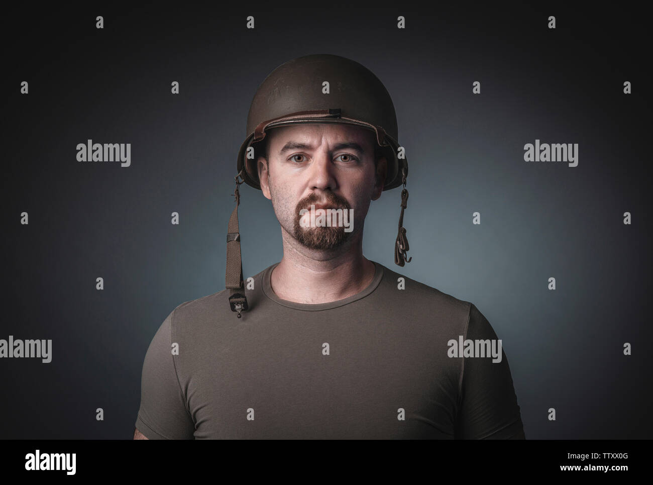 Ritratto di un uomo in una t-shirt indossando un soldato della giunta militare del casco, fissando la telecamera. Foto Stock