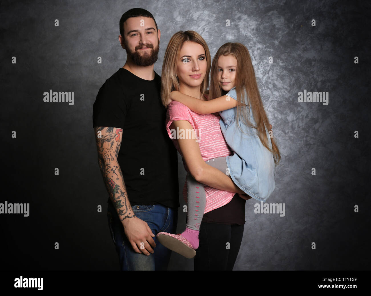 Giovane e bella famiglia con figlia sul muro grigio sfondo Foto Stock