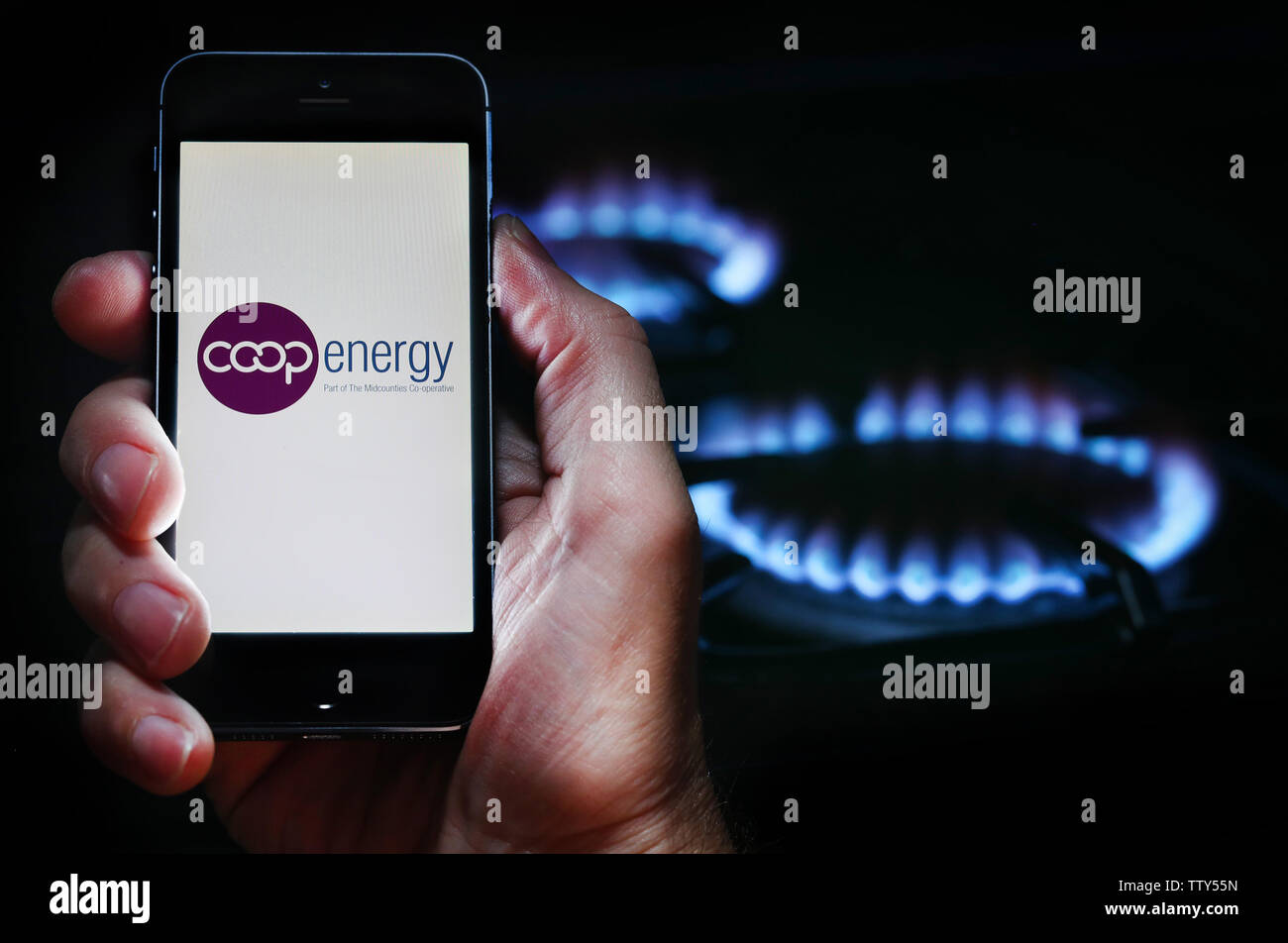 Un uomo che guarda il logo del sito web per la società di energia energia Coop sul suo telefono cellulare nella parte anteriore della sua cucina a gas (solo uso editoriale) Foto Stock