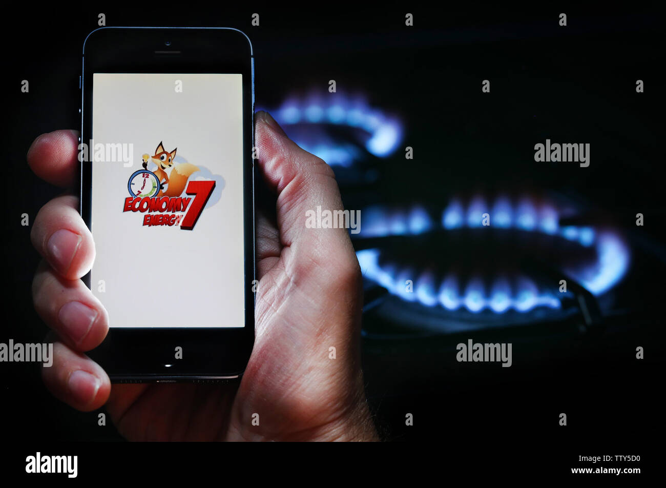 Un uomo che guarda il logo del sito web per l'energia economia aziendale 7 Energia sul suo telefono nella parte anteriore della sua cucina a gas (solo uso editoriale) Foto Stock