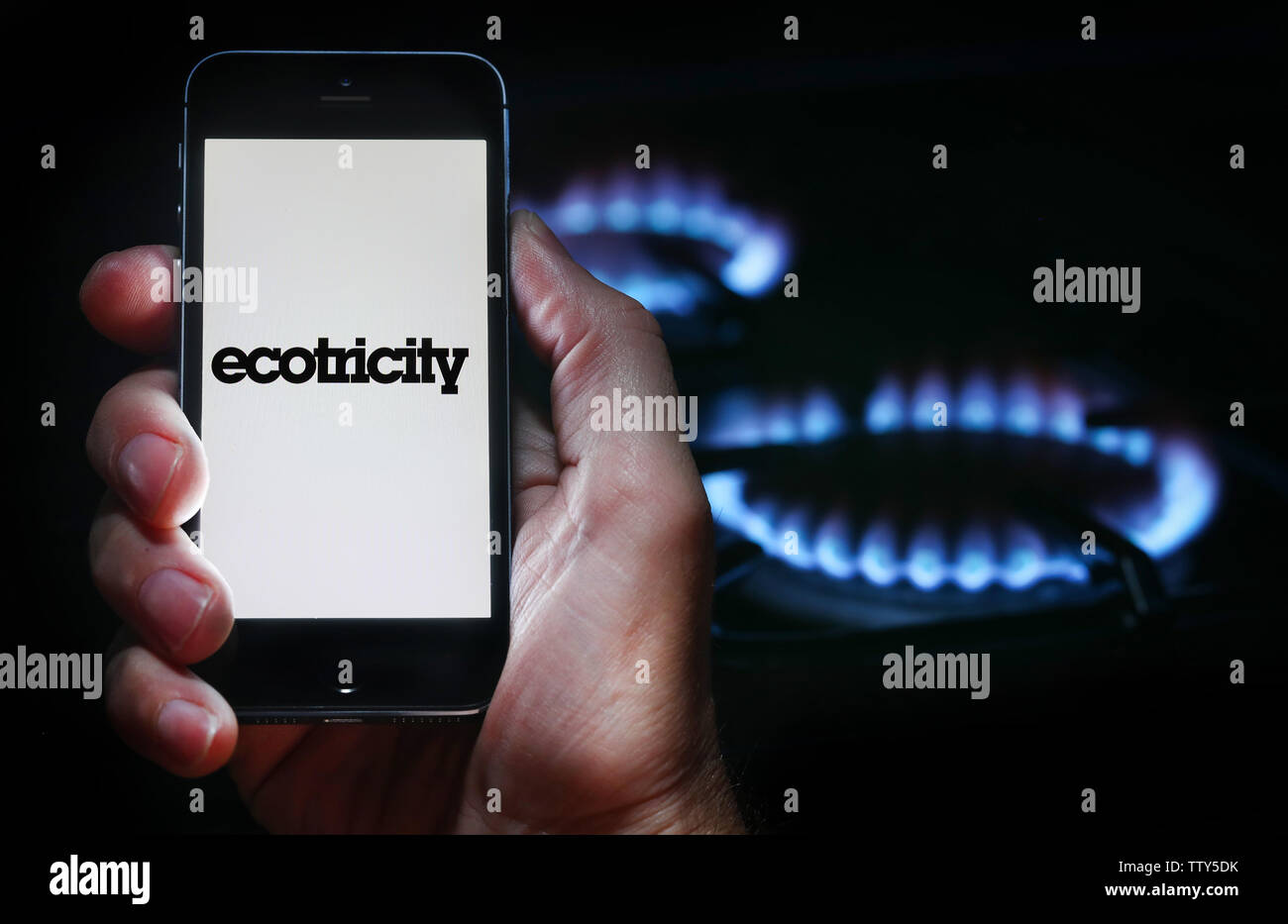 Un uomo che guarda il logo del sito web per l'energia azienda Ecotricity sul suo telefono cellulare nella parte anteriore della sua cucina a gas (solo uso editoriale) Foto Stock