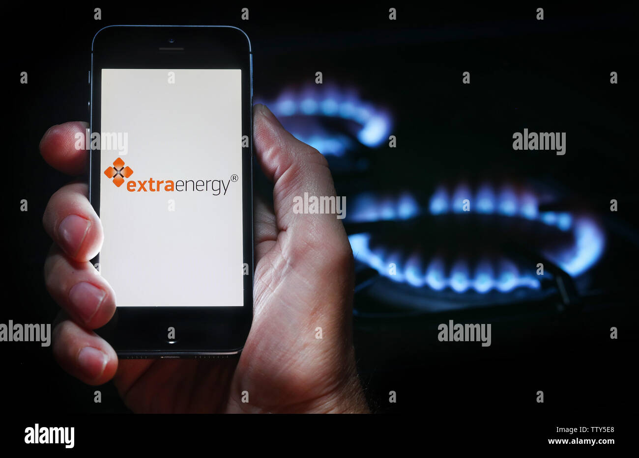 Un uomo che guarda il logo del sito web per azienda di energia Energia Extra sul suo telefono cellulare nella parte anteriore della sua cucina a gas (solo uso editoriale) Foto Stock