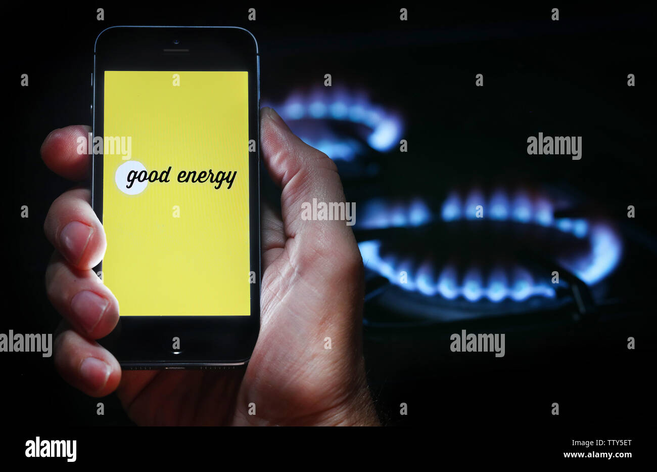 Un uomo che guarda il logo del sito web per azienda di energia una buona energia sul suo telefono cellulare nella parte anteriore della sua cucina a gas (solo uso editoriale) Foto Stock