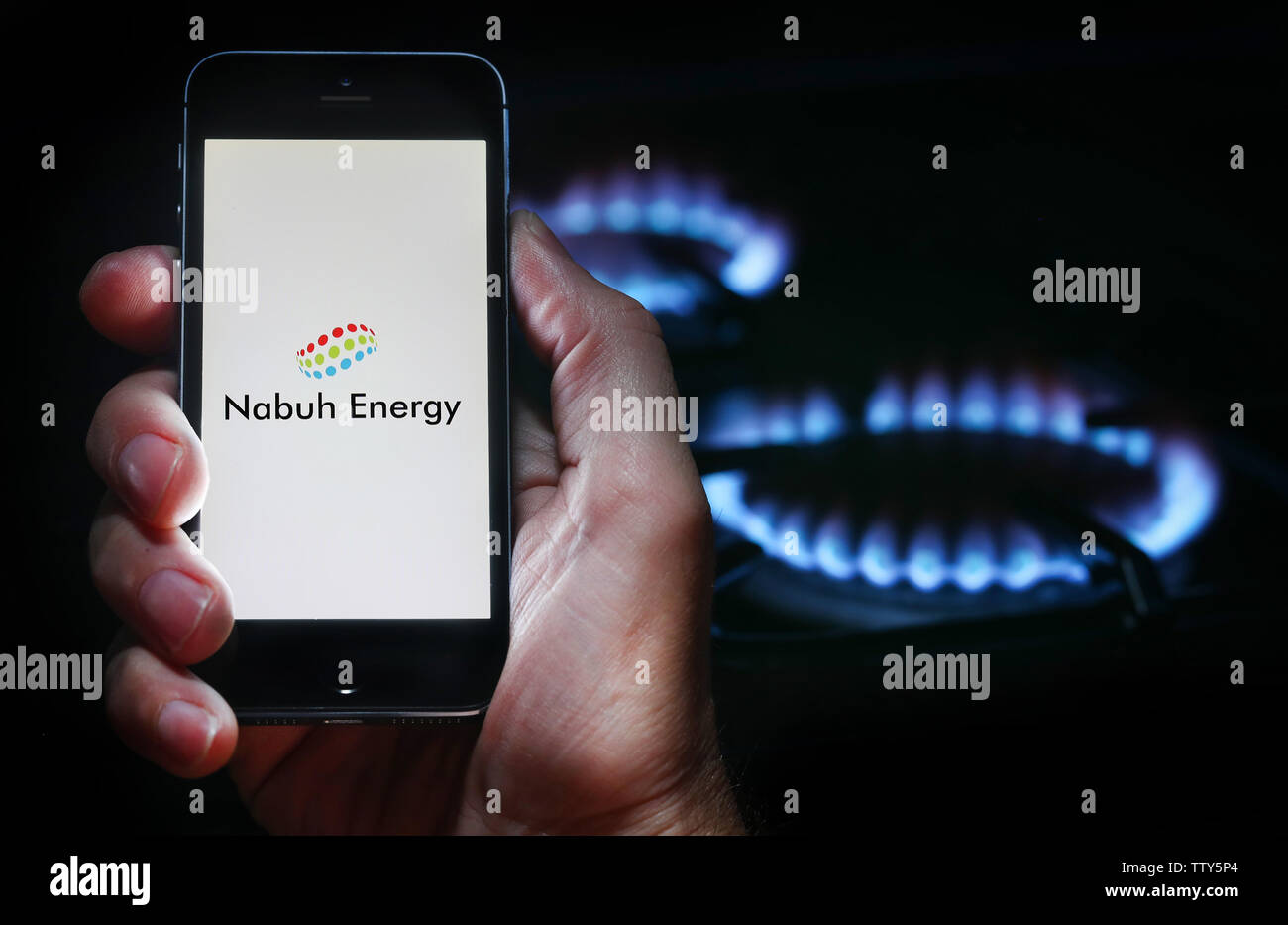 Un uomo che guarda il logo del sito web per la società di energia energia Nabuh sul suo telefono cellulare nella parte anteriore della sua cucina a gas (solo uso editoriale) Foto Stock