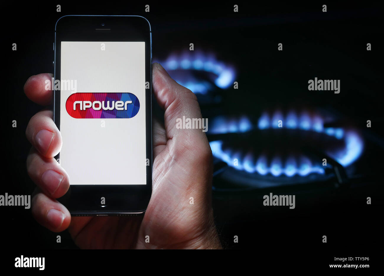 Un uomo che guarda il logo del sito web per la società energetica NPower sul suo telefono cellulare nella parte anteriore della sua cucina a gas (solo uso editoriale) Foto Stock