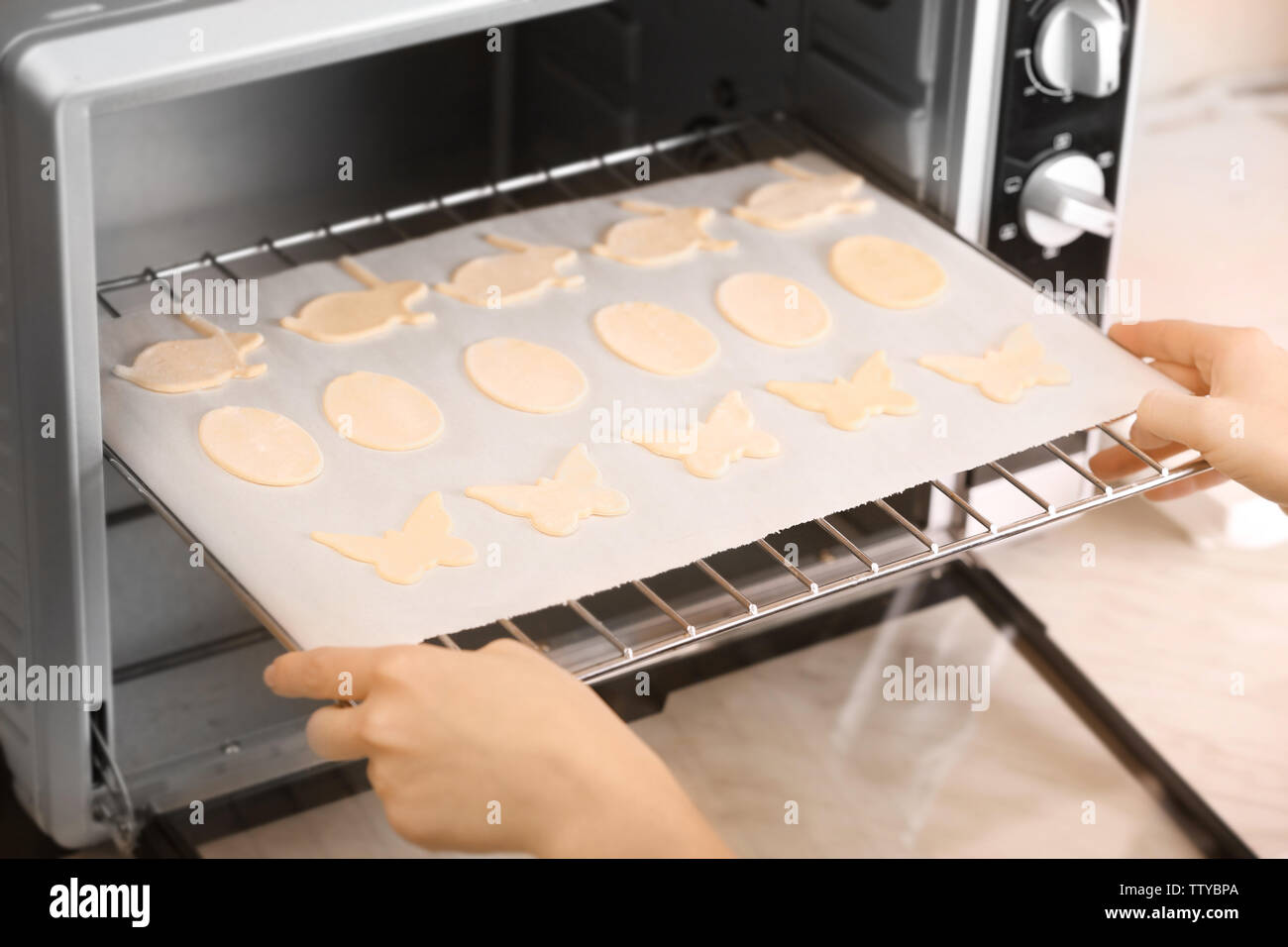 Donna mettendo la griglia da forno con materie Pasqua i cookie in forno, primo piano Foto Stock
