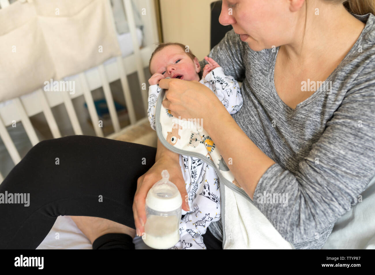 Giovane madre alimentazione neonato. Donna salviette viso infantile e feed dalla bottiglia di latte Foto Stock