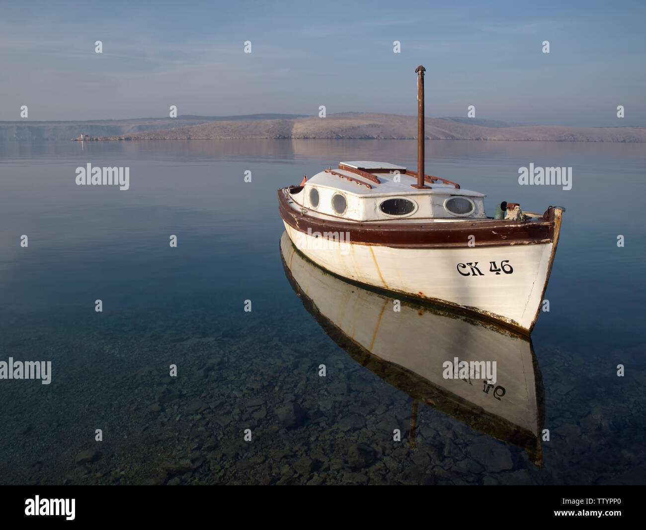 Bianco barca riflessa sulla calma superficie del mare con il cielo blu, il blu del mare e terra in background. Shot vicino a Crikvenica, Croazia Foto Stock