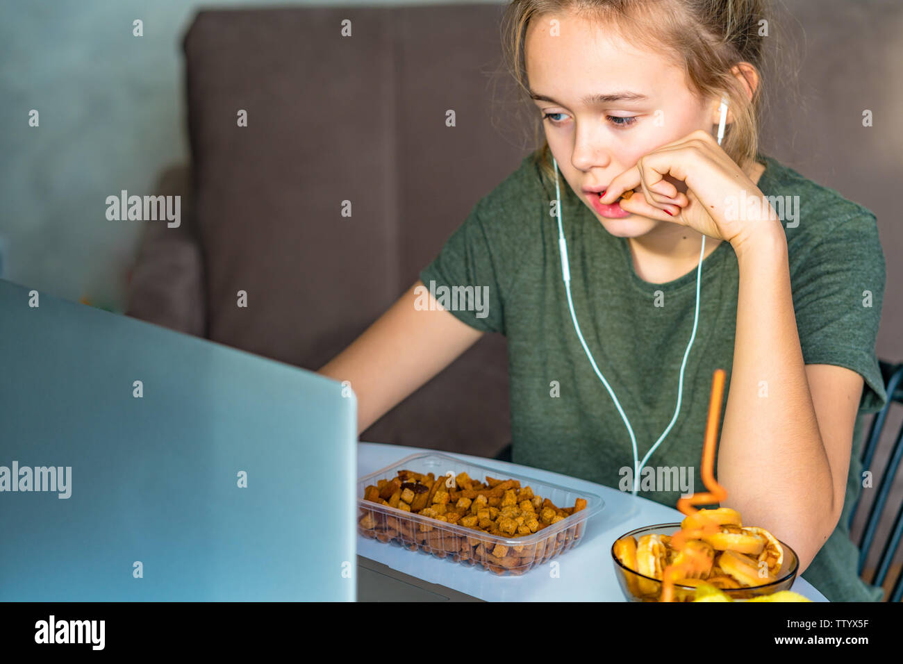 Ragazza lavora a un computer e si mangia il fast food. Cibo malsano: chips, cracker, candy, waffle, cola. Il cibo spazzatura, concetto. Foto Stock
