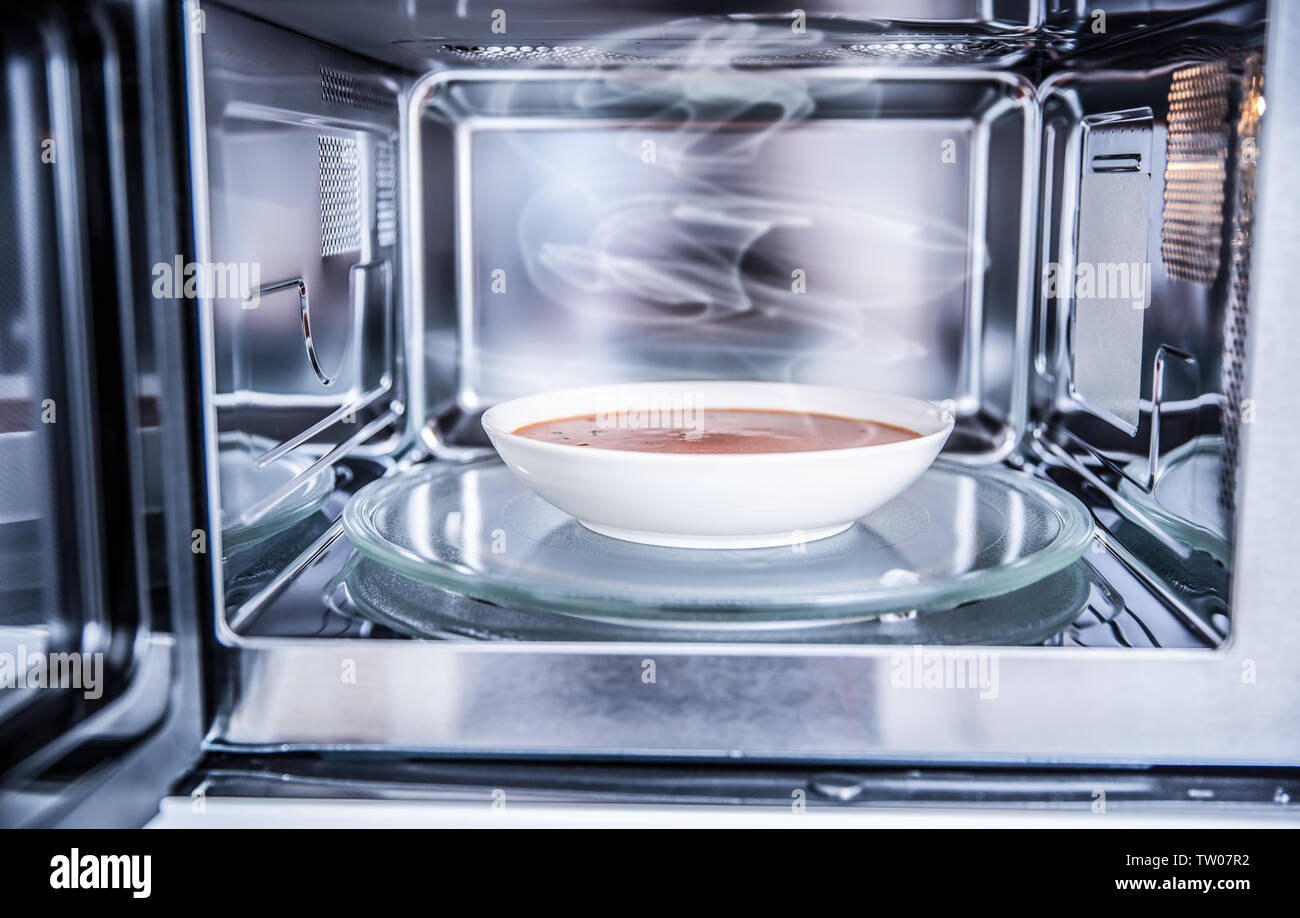 Vista interna di nuovo pulita staniless forno a microonde con una zuppa di pomodoro in piastra bianca. Foto Stock