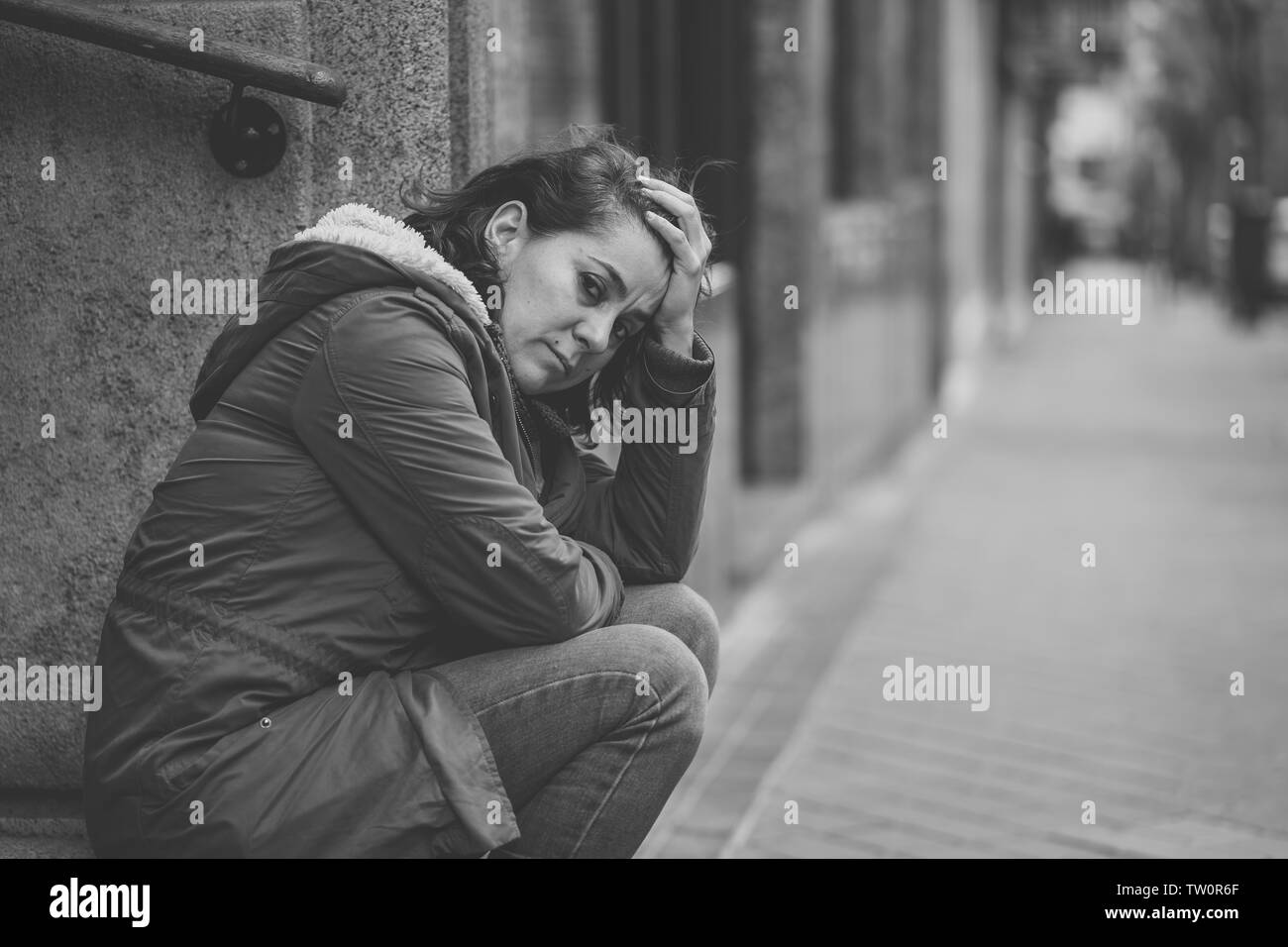 Donna attraente affetti da depressione abbattimento triste infelice heartbroken e solitaria seduta in città strada urbana in salute mentale dolore emotivo Abu Foto Stock
