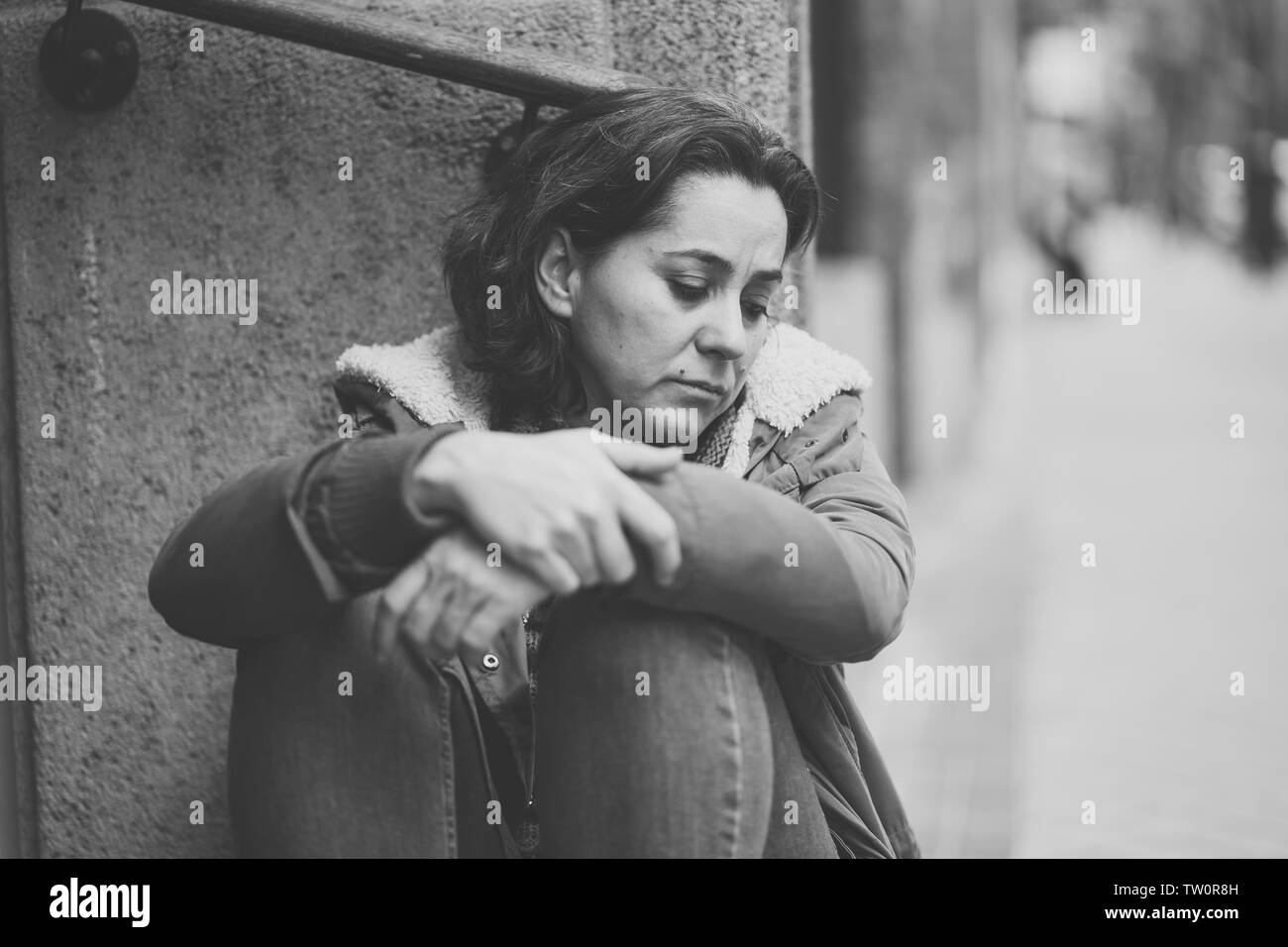 Donna attraente affetti da depressione abbattimento triste infelice heartbroken e solitaria seduta in città strada urbana in salute mentale dolore emotivo Abu Foto Stock