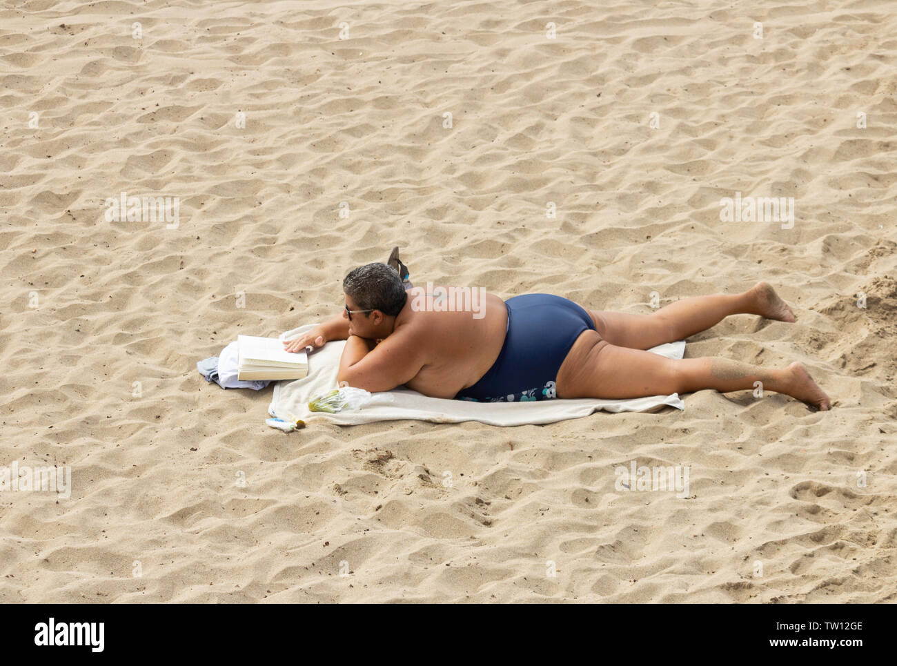 Obesi, sovrappeso donna libro di lettura sulla spiaggia in Spagna. Foto Stock