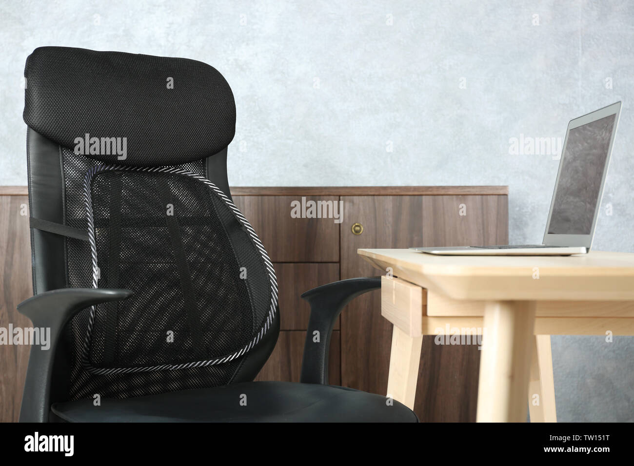 Sedia da ufficio con mesh per supporto posteriore e sul computer portatile sul tavolo, in interni Foto Stock