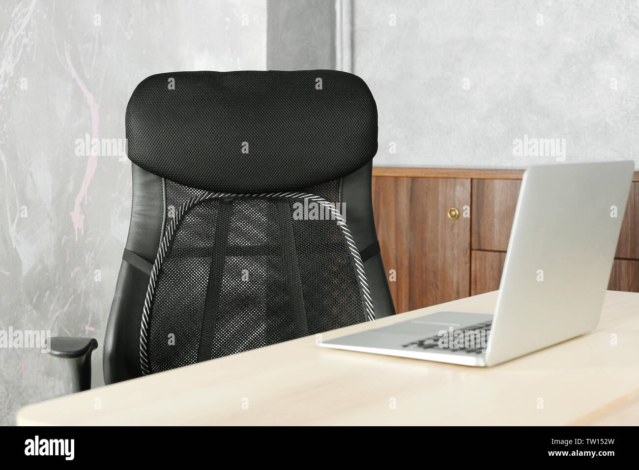 Sedia da ufficio con mesh per supporto posteriore e sul computer portatile sul tavolo, in interni Foto Stock