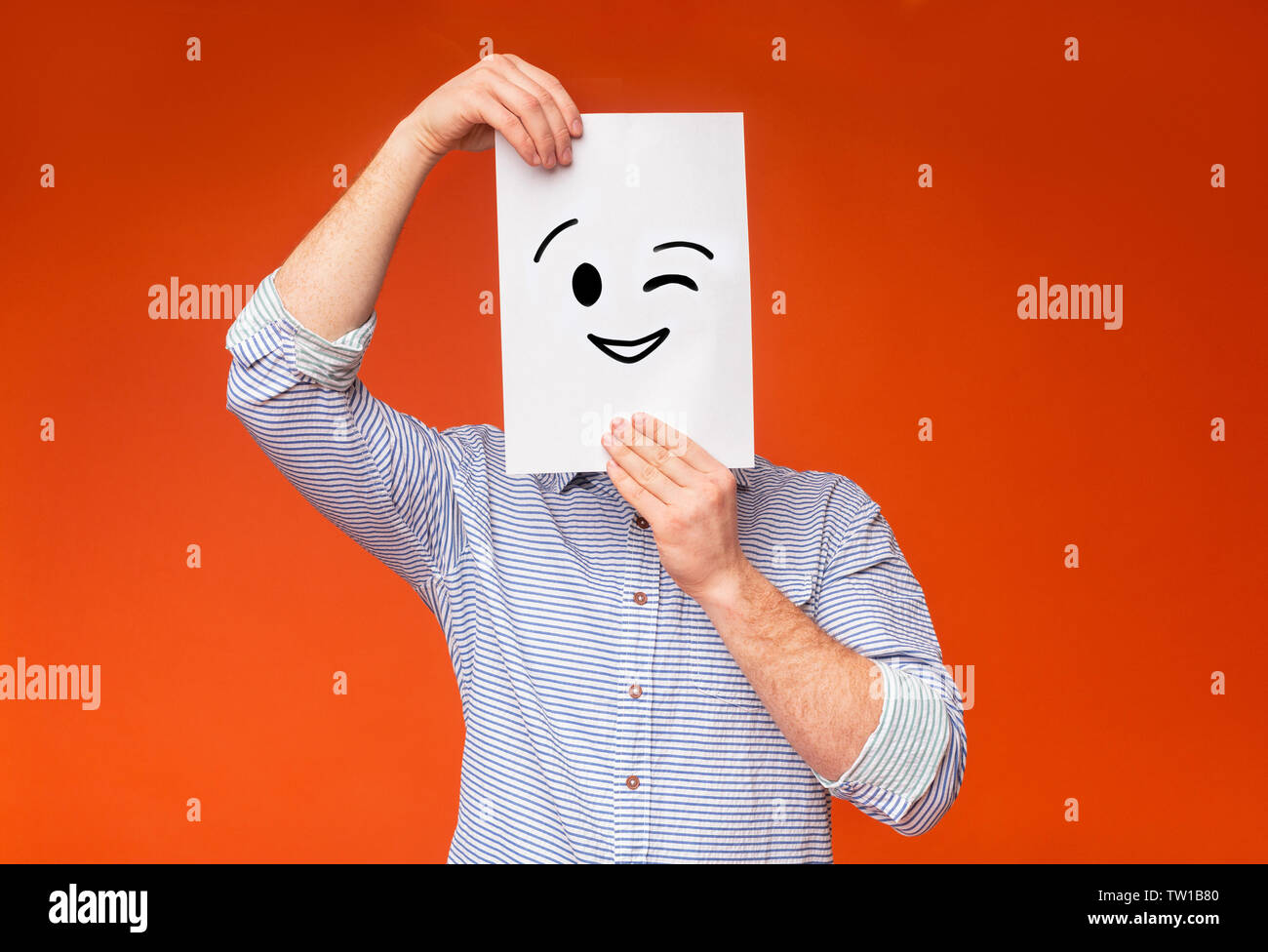 Giovane ragazzo nasconde la sua faccia sotto dipinto winking sorriso sul libro bianco, sfondo arancione, panorama Foto Stock