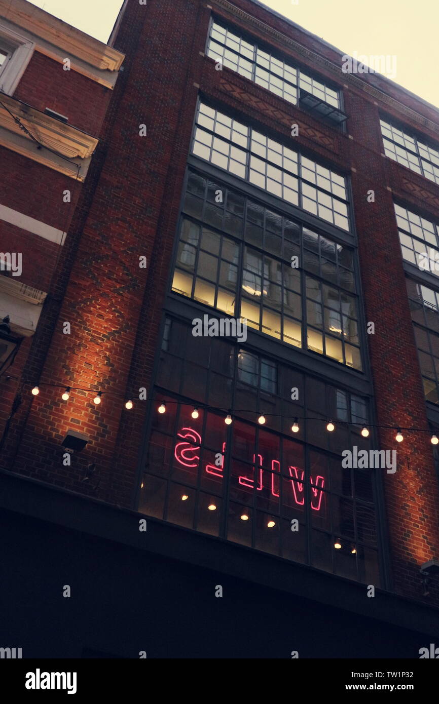 Una casa di mattoni in un stile industriale in Londra, Regno Unito. In una finestra si illumina di un colore rosa segno al neon. Davanti a questo è presente una luce stringa, che si illumina come bene. Foto Stock