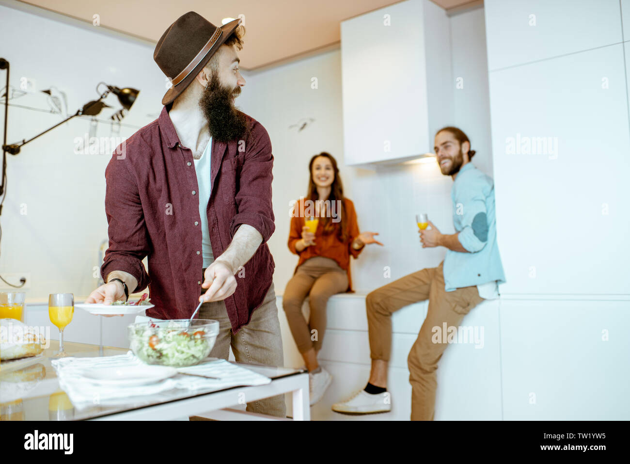 Giovani amici di parlare e avendo alcuni snack durante la riunione sulla cucina a casa Foto Stock
