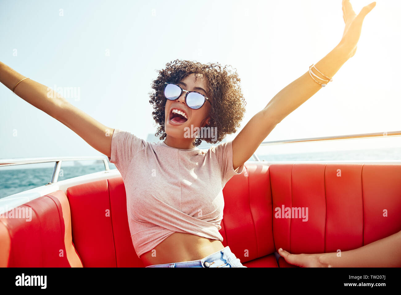 Ridendo giovane donna seduta su una barca con le braccia sollevate in aria durante le sue vacanze estive Foto Stock