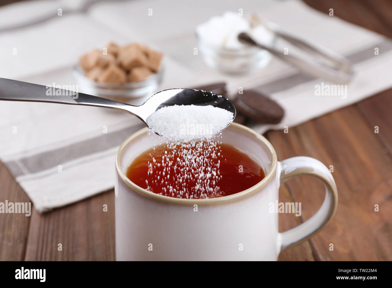 Aggiunta di zucchero per tazza di tè nero sul tavolo di legno Foto Stock