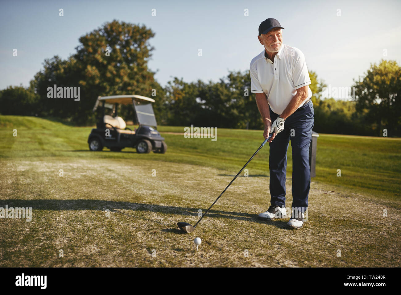 Sportivo da uomo senior in procinto di fare un colpo con il suo autista durante la riproduzione di un round di golf in una giornata di sole Foto Stock