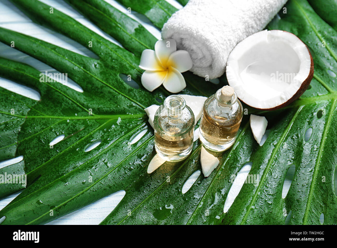 Le bottiglie di olio di noce di cocco, asciugamano, fiore tropicale sulla foglia verde Foto Stock