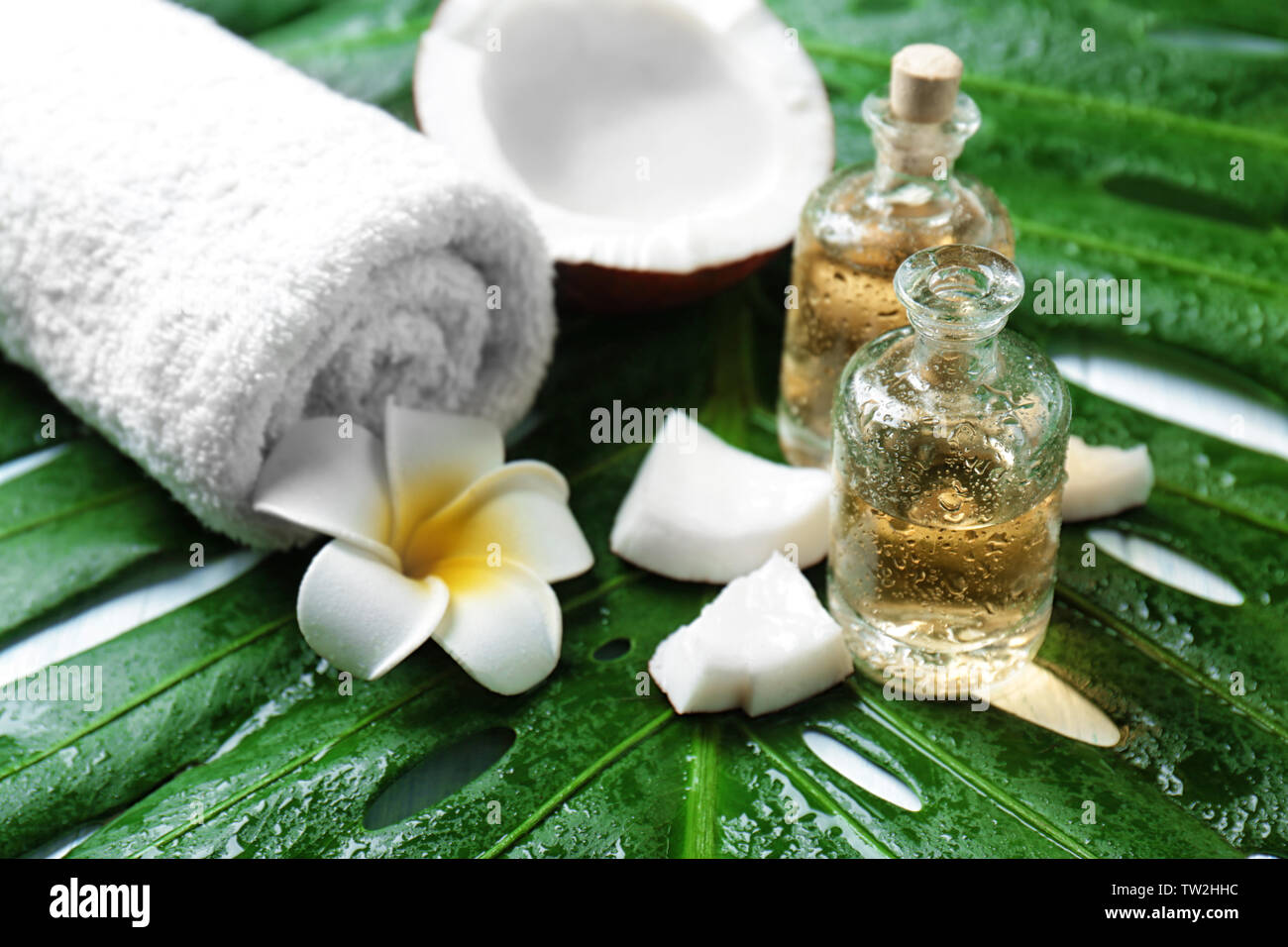 Le bottiglie di olio di noce di cocco, asciugamano, fiore tropicale e di foglia, primo piano Foto Stock