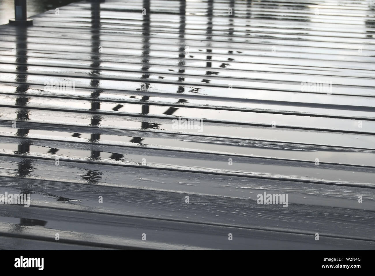 Pozze di acqua su legno pavimentazione pedonale sul giorno di pioggia, ringhiera riflessa nel pavimento bagnato Foto Stock