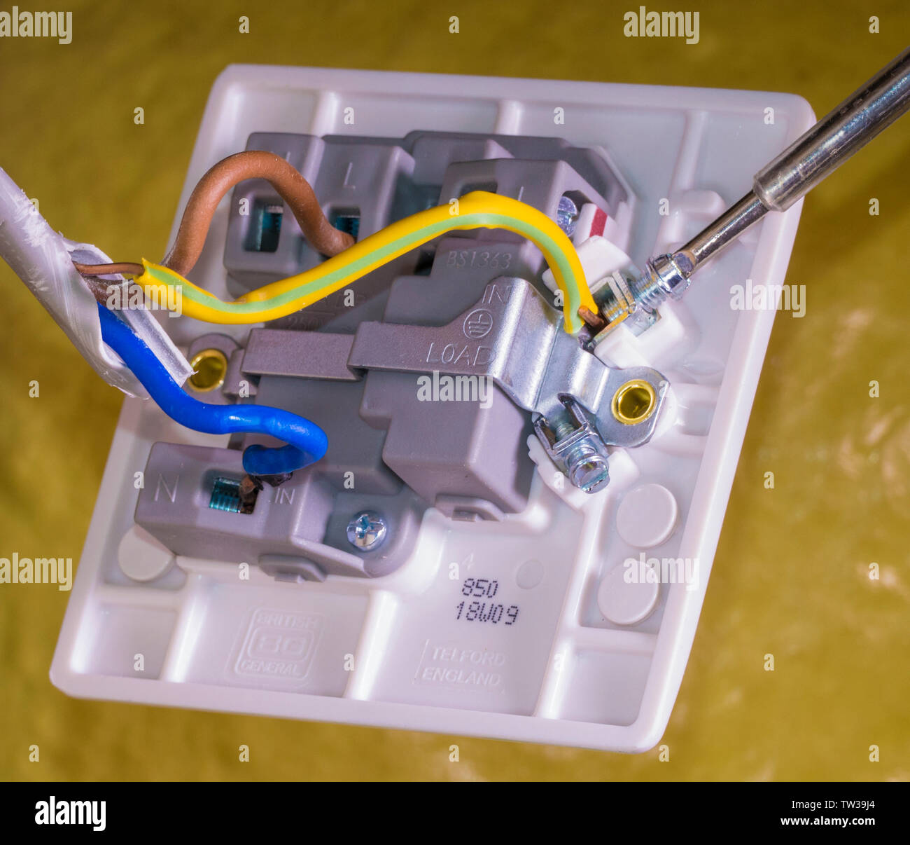 Dettaglio dei collegamenti per il blu, marrone e verde/giallo, i fili con un cacciavite su un terminale, dietro l'interruttore on/off per un Regno Unito apparecchio standard. Foto Stock