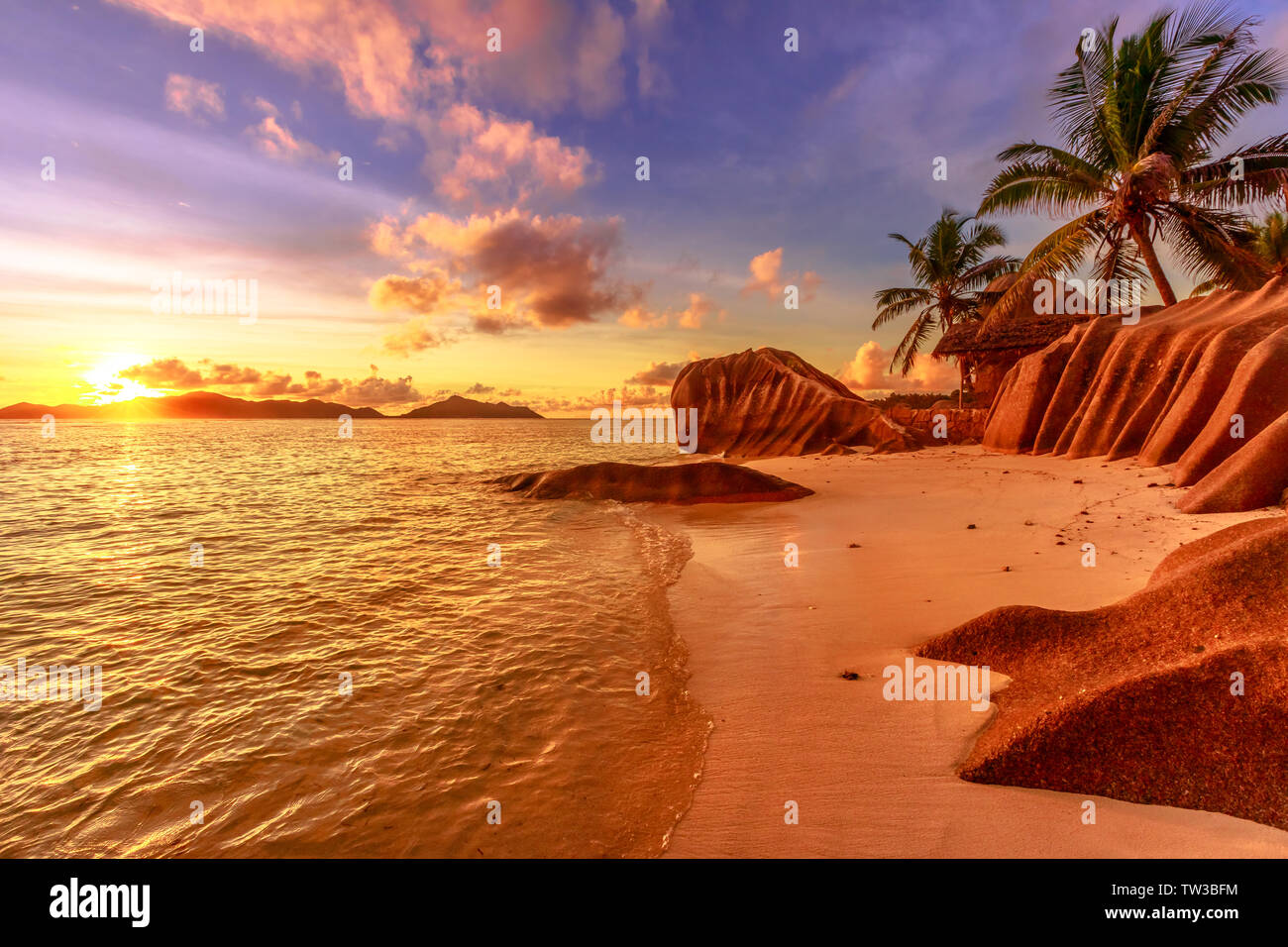 Seychelles, La Digue, Anse Source d'Argent al tramonto. Paesaggio con cielo e le nuvole colorate su roccia in pietra di granito con palme. Sun al crepuscolo Foto Stock