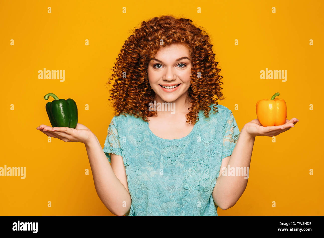 Carino dai capelli ricci donna azienda grande giallo fresco e pepe verde nelle sue mani su sfondo giallo Foto Stock