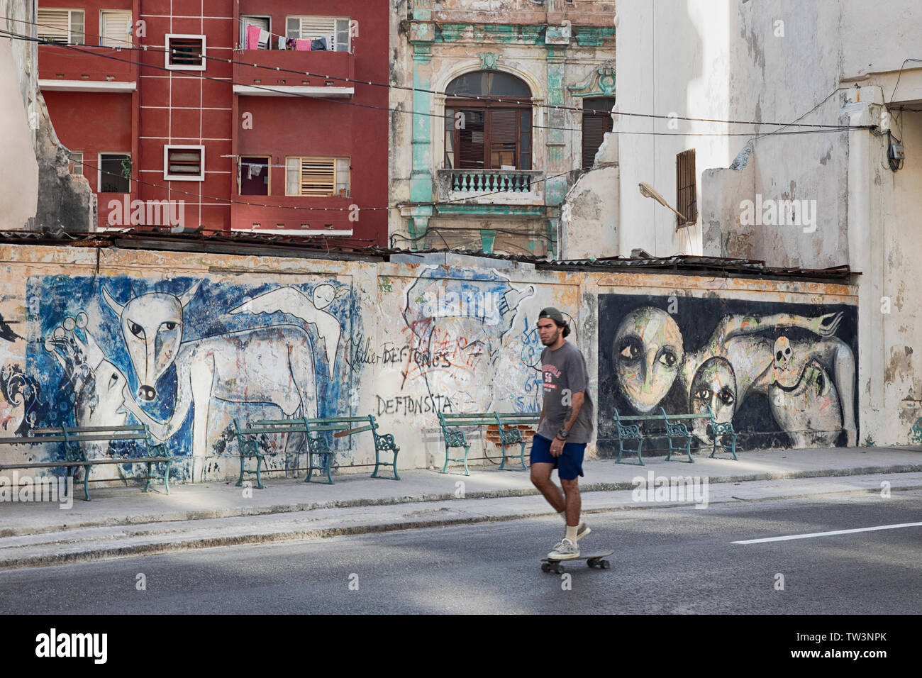 Un guidatore di skateboard pattinaggio passato edifici fatiscenti con graffiti sulle pareti in Paseo de Marti Havana Cuba. Foto Stock