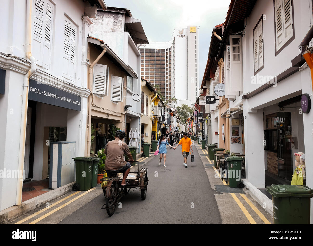 Un vecchio uomo cavalca un triciclo con una consegna di pacchi carrello collegato alla parte anteriore lungo Haji lane in Singapore. Foto Stock