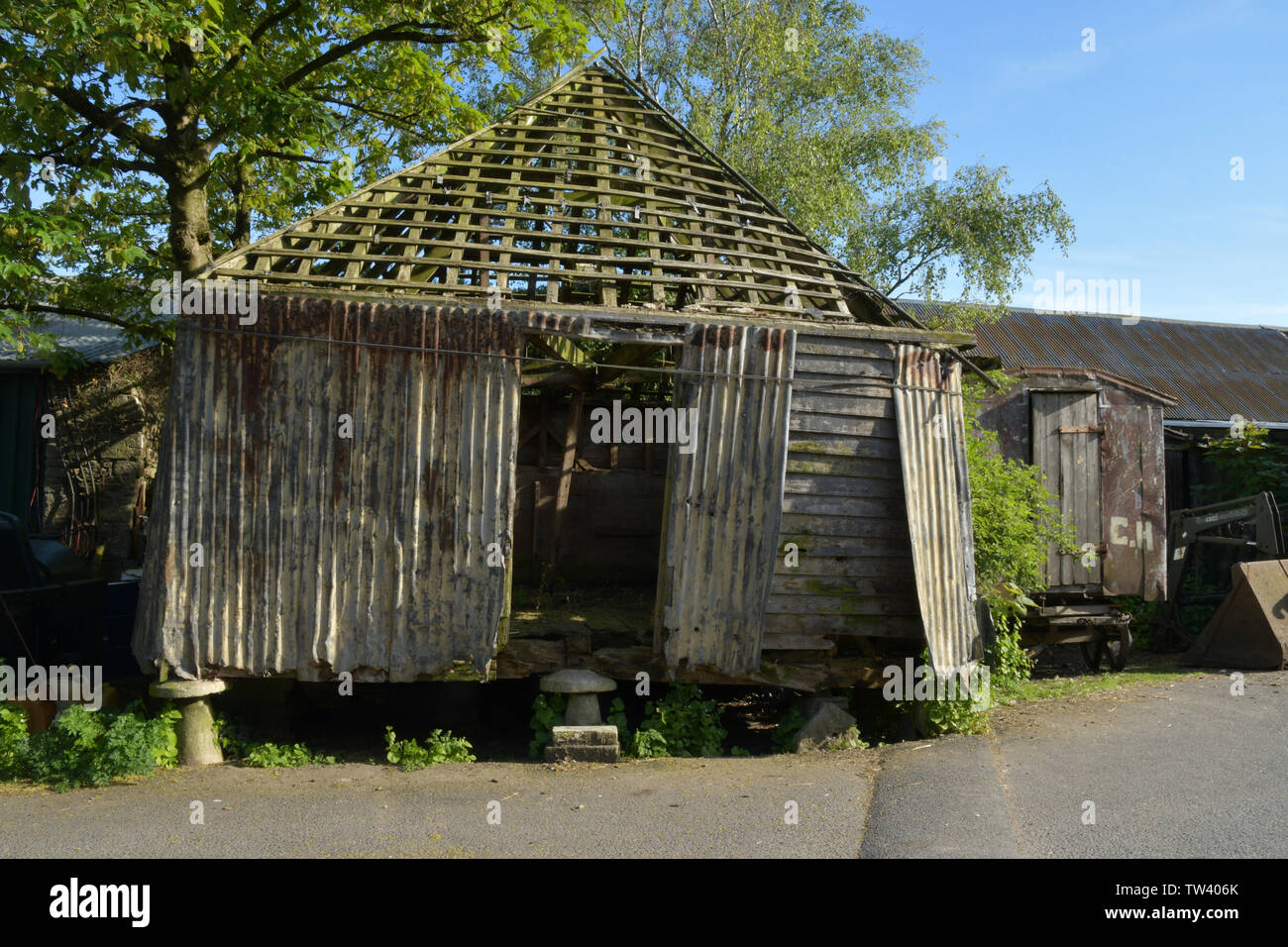 Vecchia fattoria grain store su pietre staddle.legno e ferro corrugato costruzione. Piastrelle rimosse per il riutilizzo e il casolare tenuti insieme con la fune.Old ella con ruote Foto Stock