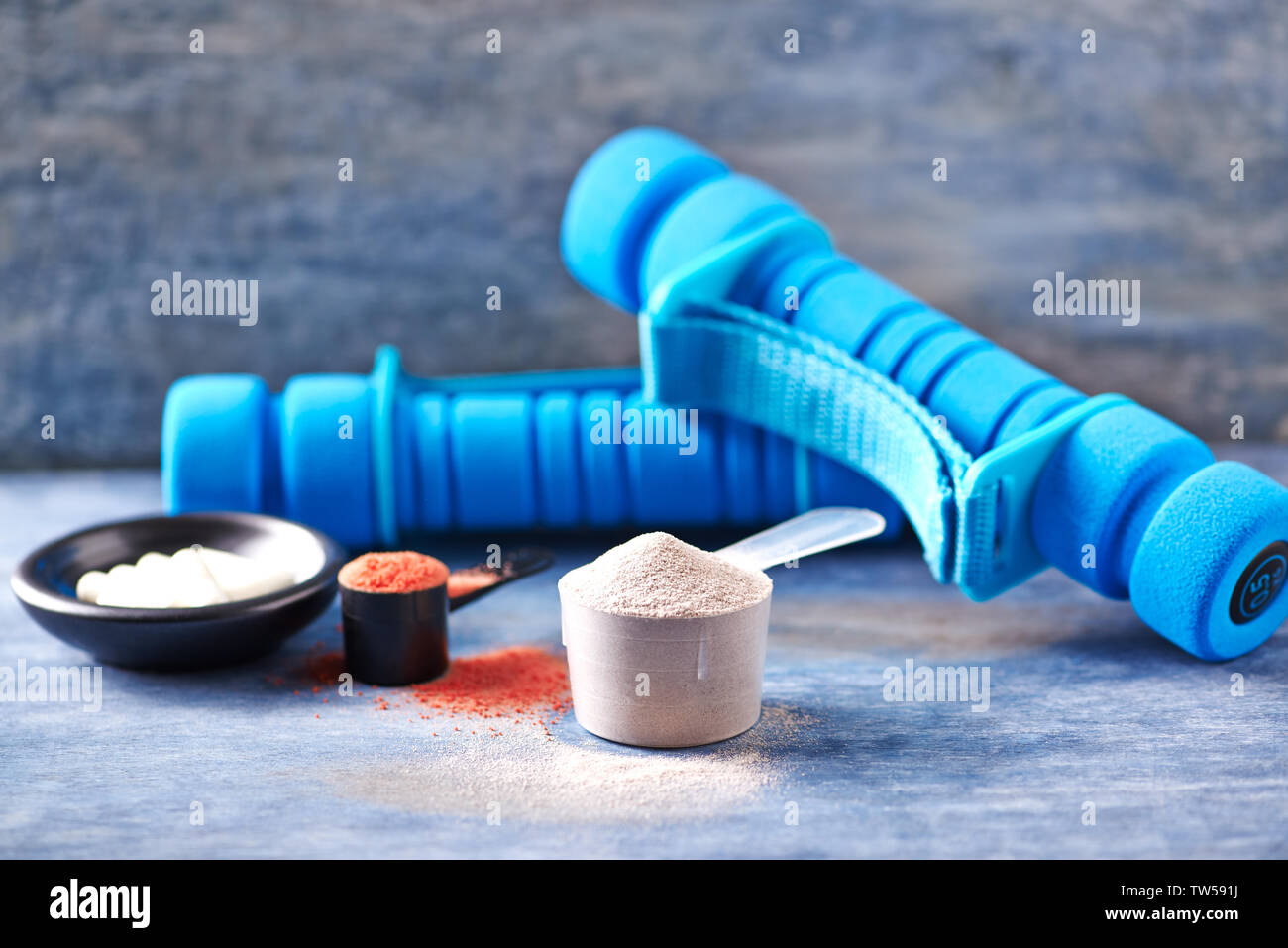 La creatina in polvere, Scoop di proteina del siero di latte, taurina  capsule blu e manubri in background Foto stock - Alamy