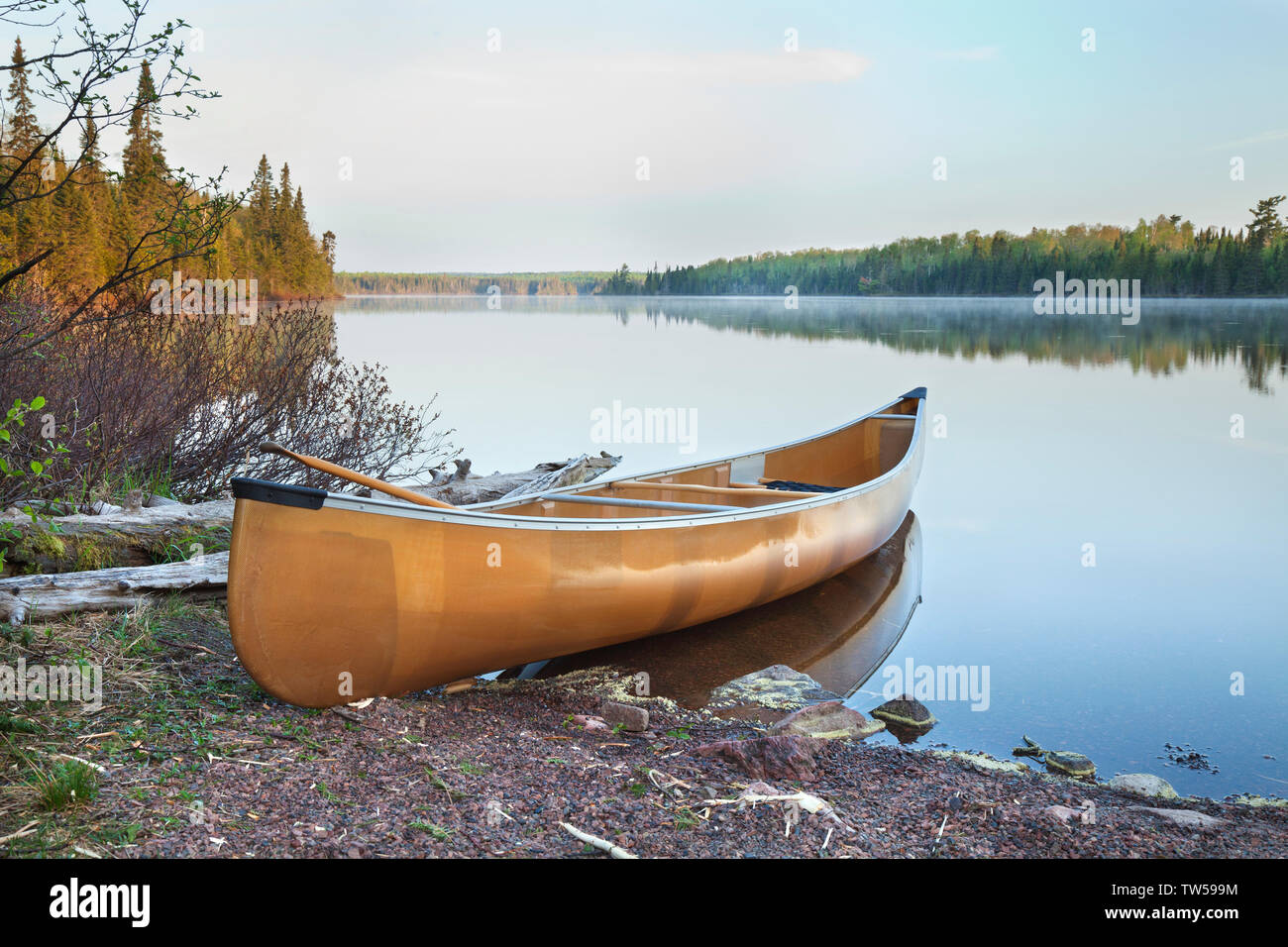 Canoa gialla sulla riva di una calma nord del Minnesota e il lago di prima mattina la luce Foto Stock