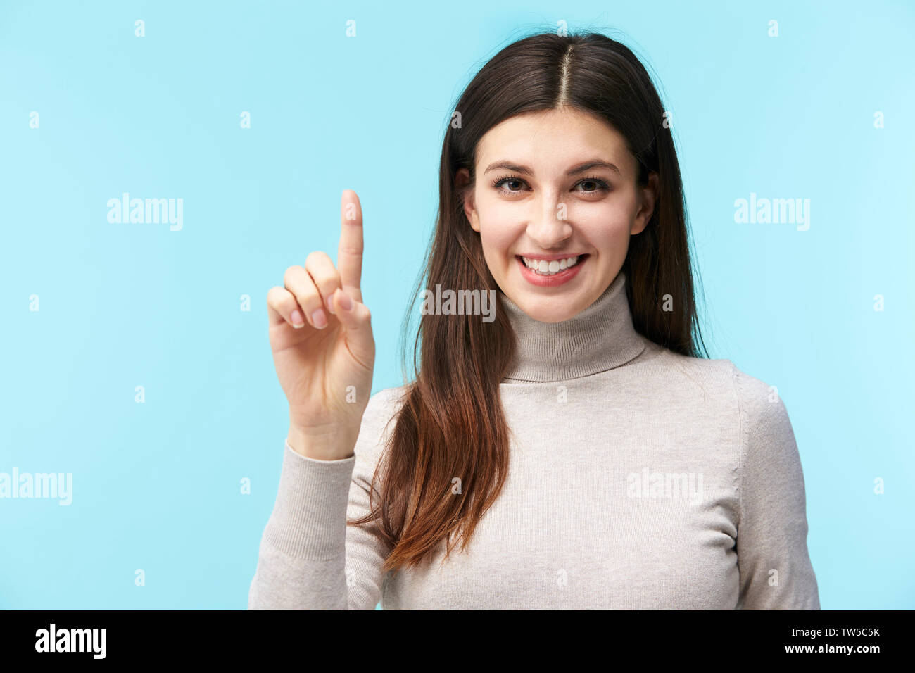 Bellissima giovane donna caucasica premendo un tasto virtuale, guardando la telecamera sorridendo, isolato su sfondo blu Foto Stock
