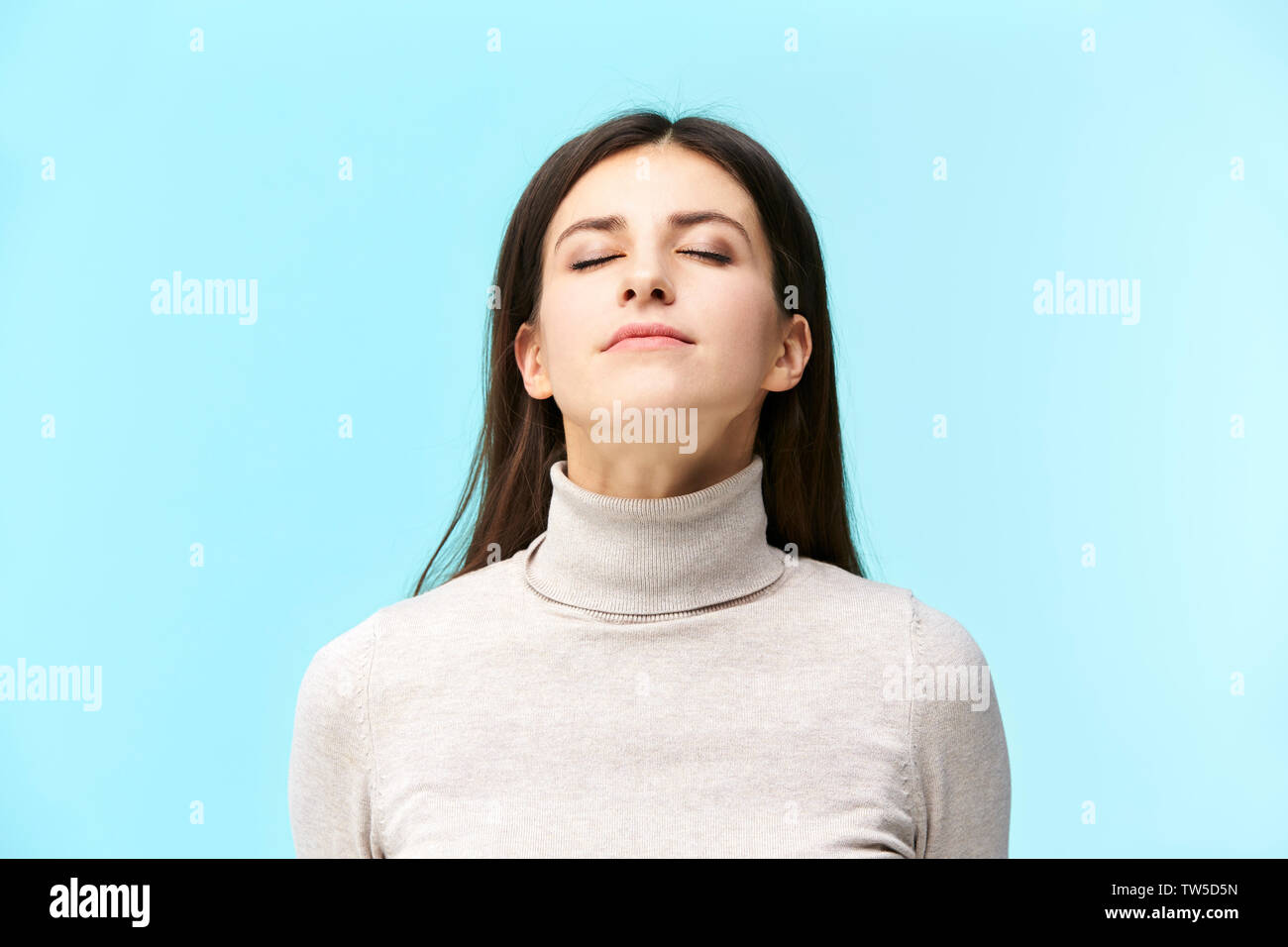 Ritratto di una giovane e bella donna caucasica a occhi chiusi, odorando la fragranza nell'aria, isolato su sfondo blu Foto Stock