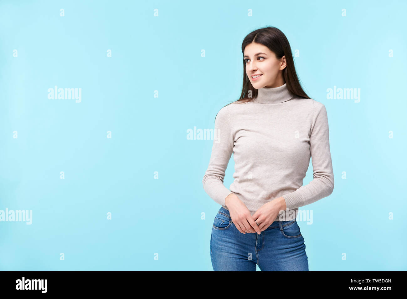Ritratto di una giovane e bella donna caucasica, in piedi, guardando lontano e sorridente, isolato su sfondo blu Foto Stock