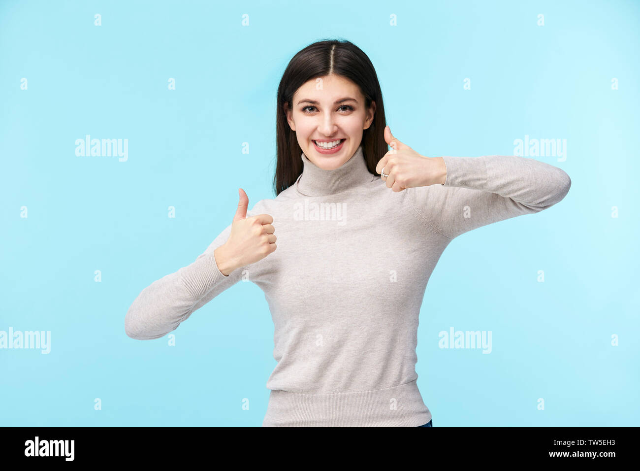 Ritratto di una giovane e bella donna caucasica con due dita verso l'alto, guardando la telecamera sorridendo, isolato su sfondo blu Foto Stock