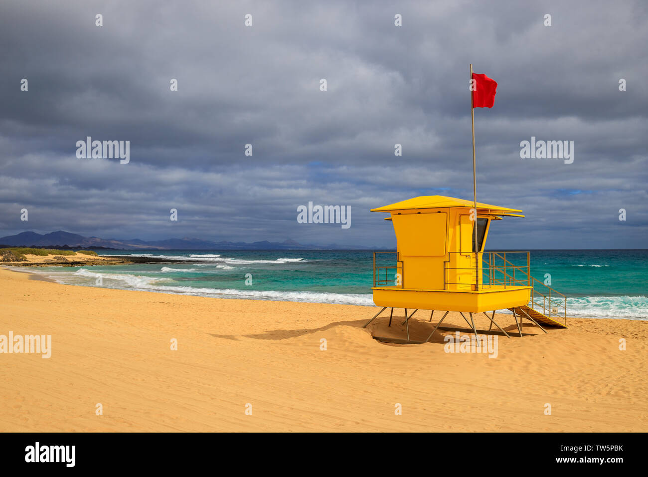 Bellissima spiaggia con un bagnino torre in primo piano con una bandiera rossa. Colori saturi in un giorno nuvoloso Foto Stock