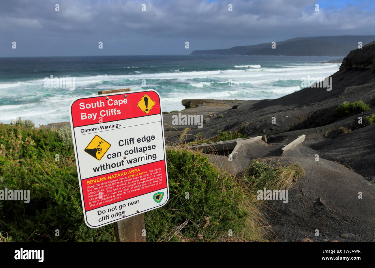 Segnale di avvertimento a sud Cape Bay scogliere a sud della Baia del Capo nel Sud Tasmania con Oceano Meridionale e onde da surf in background. Foto Stock