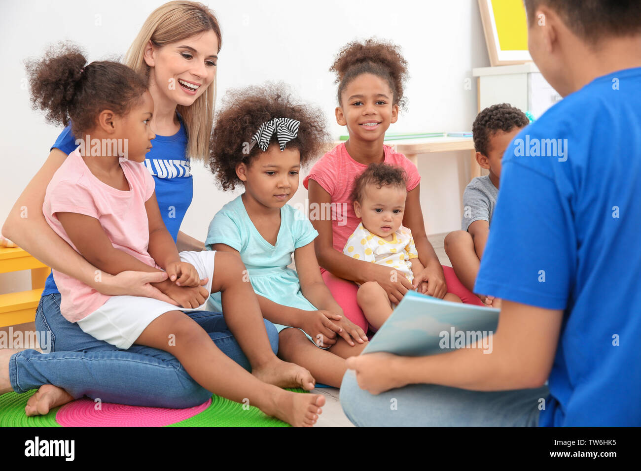 I giovani volontari libro di lettura con bambini piccoli nella camera di luce. Il volontariato all'estero concetto Foto Stock