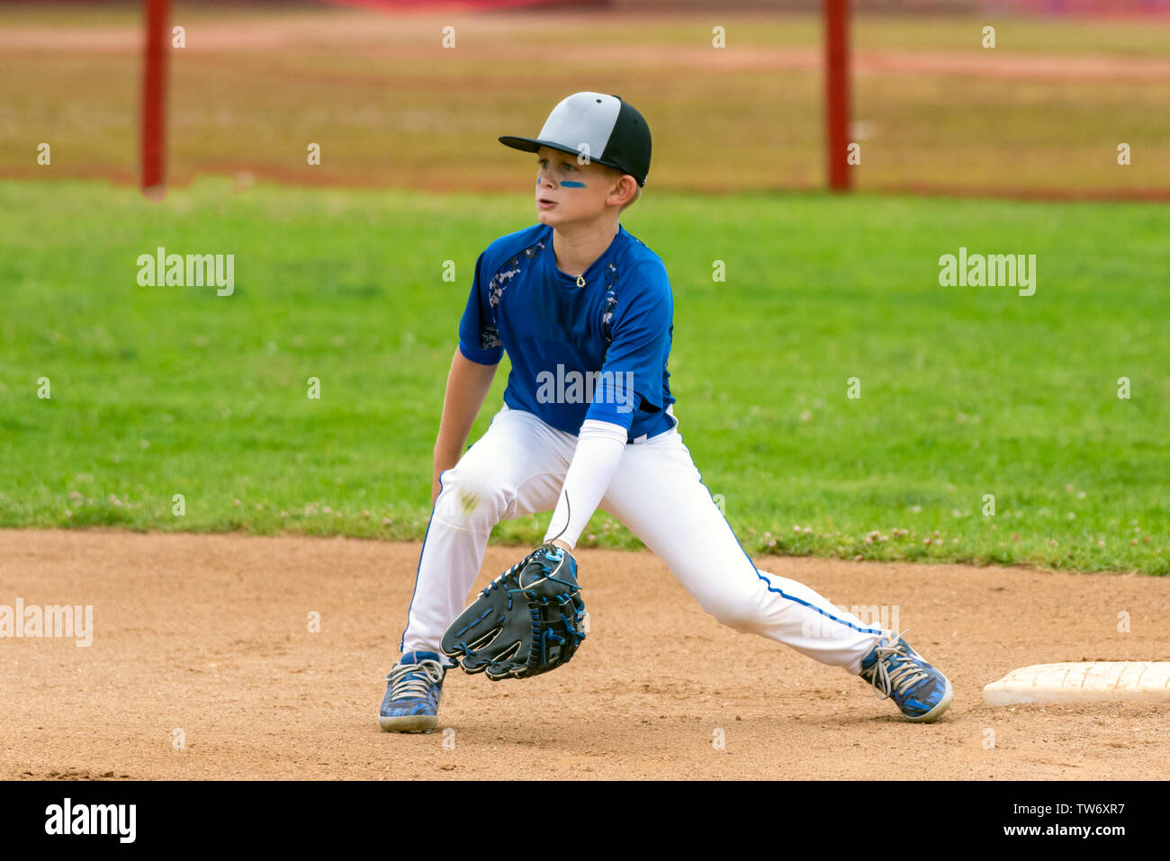 La gioventù giocatore di baseball in uniforme blu che copre la seconda base e attesa per la sfera nell'infield durante una partita. Foto Stock