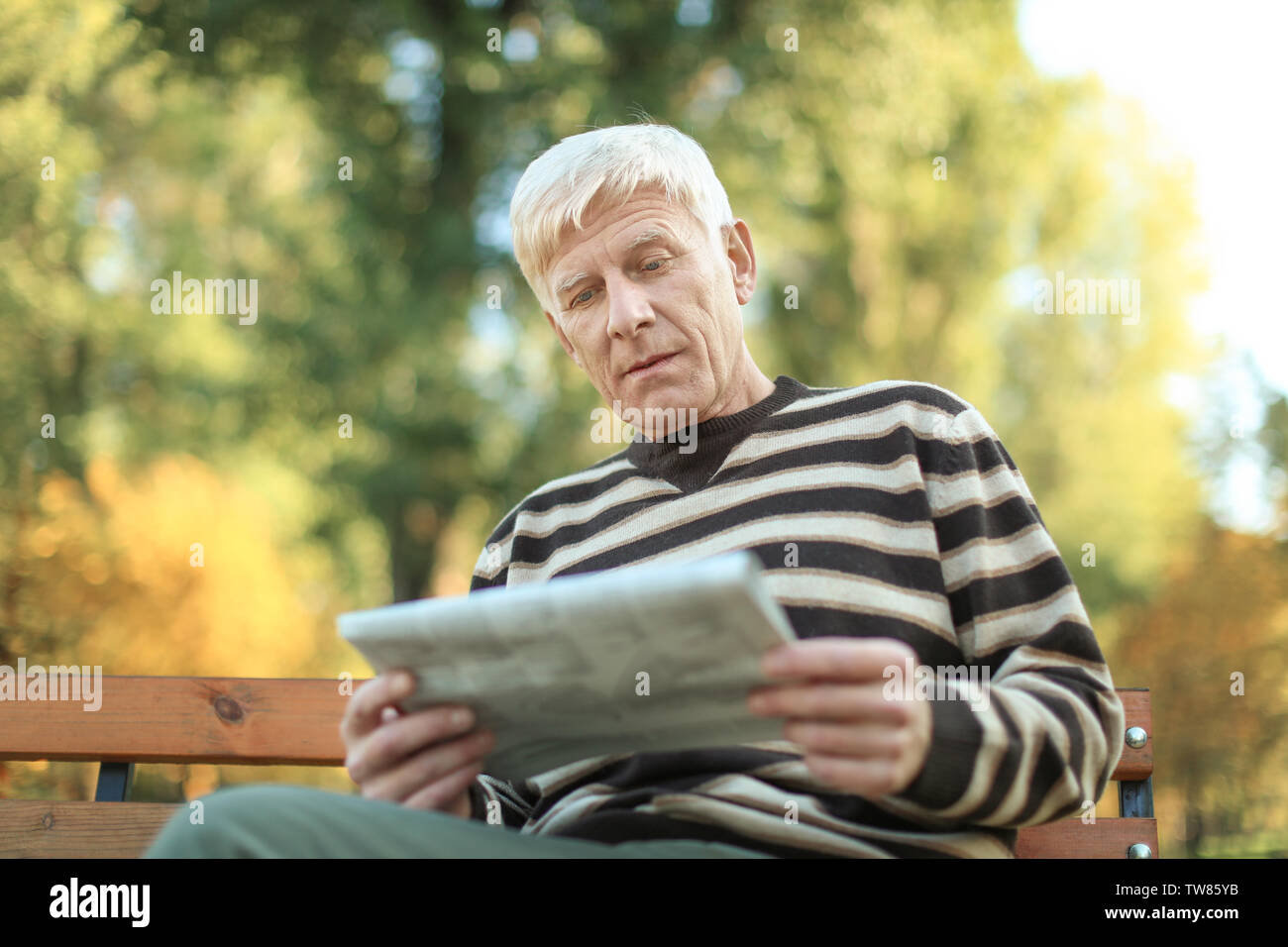 Elegante uomo maturo seduta sul banco e leggere il giornale in autunno park Foto Stock