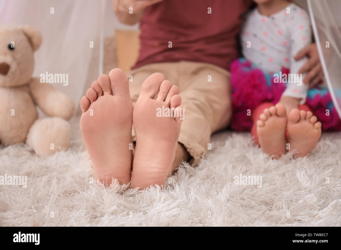 A piedi nudi padre e sua figlia piccola seduta sul tappeto a casa Foto Stock