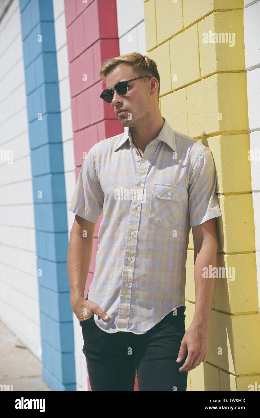 Un modello maschio biondo che indossa una camicia a quadri occidentale, che si posa contro una parete in piedi all'aperto. Foto Stock