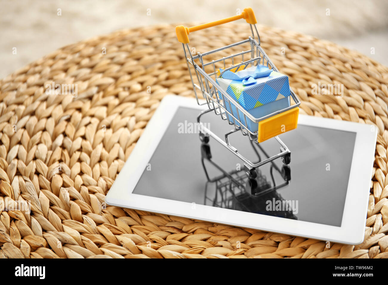 Tablet PC e piccolo carrello con confezione regalo sul pouf in vimini. Internet il concetto di shopping Foto Stock