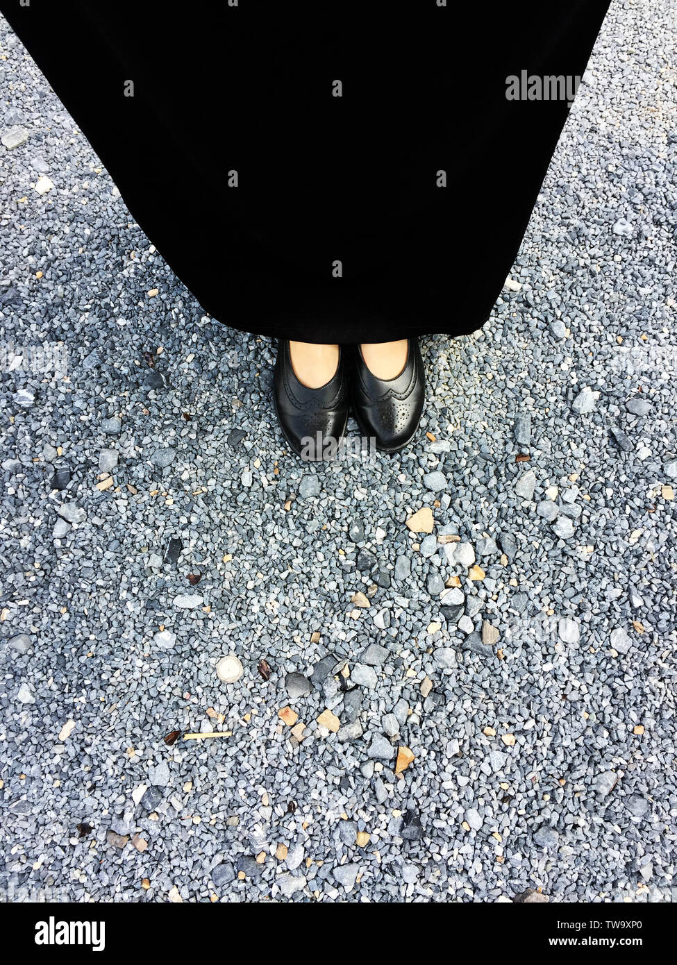 Donna indossare nero tacco alto su sfondo di cemento. Vista dall'alto giovane e bella donna che indossa scarpe nere sul cemento. Primo piano di gambe e piedi per abiti Foto Stock