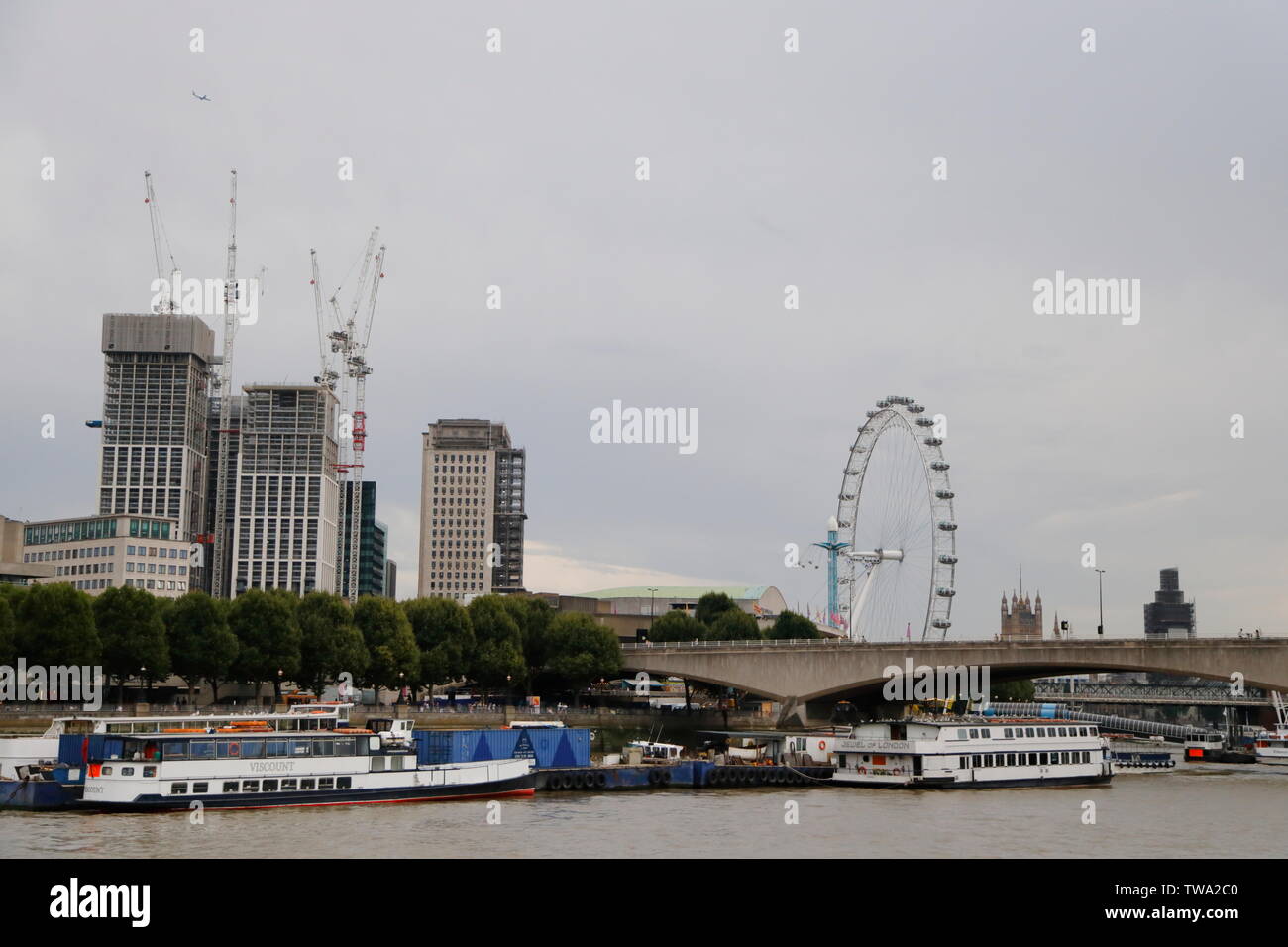 Un aereo vola sopra di Londra con il London Eye e la creazione di progetti di costruzione come si vede dal Fiume Tamigi a Londra, Regno Unito. Foto Stock